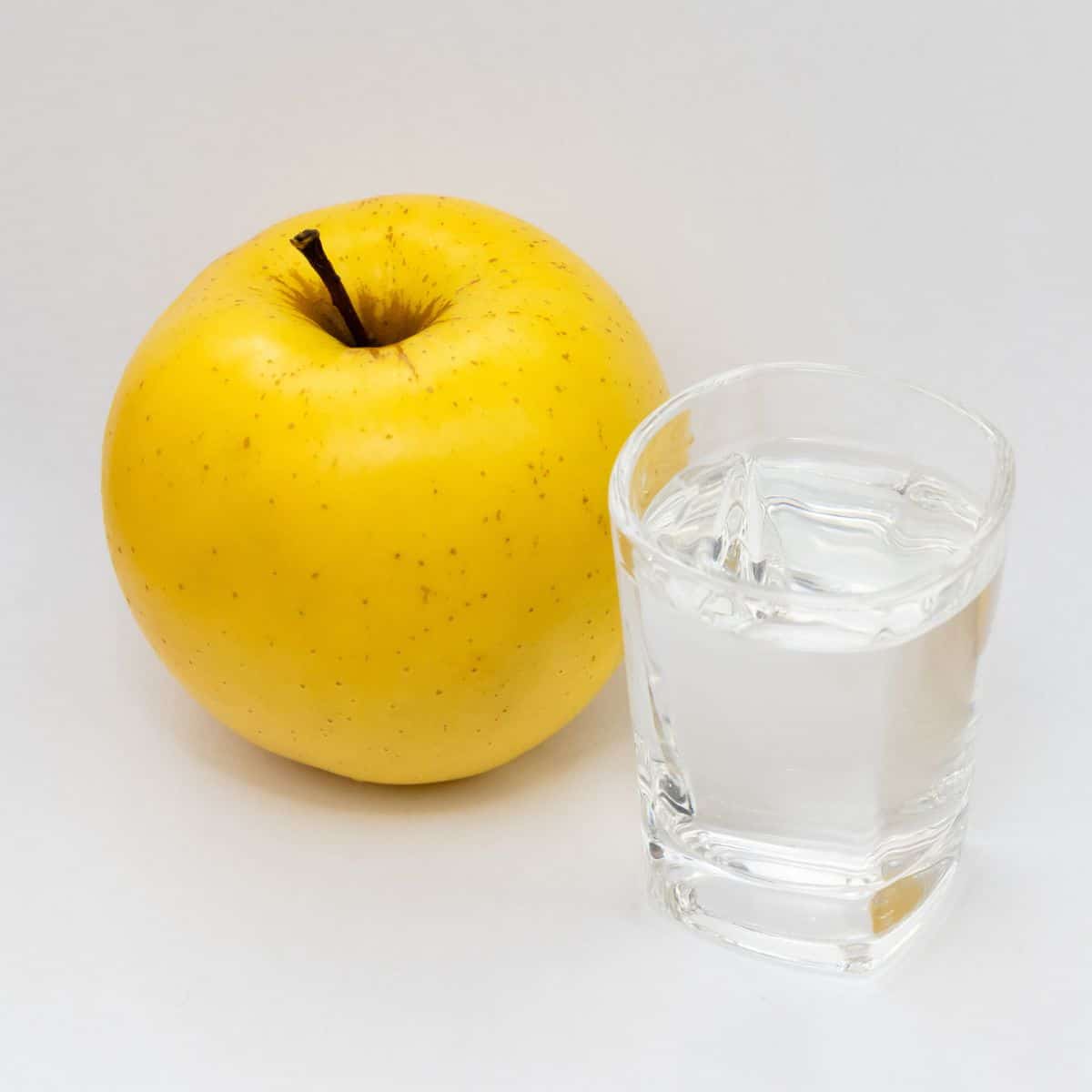 Rajka apple on a white background next to a shot glass.