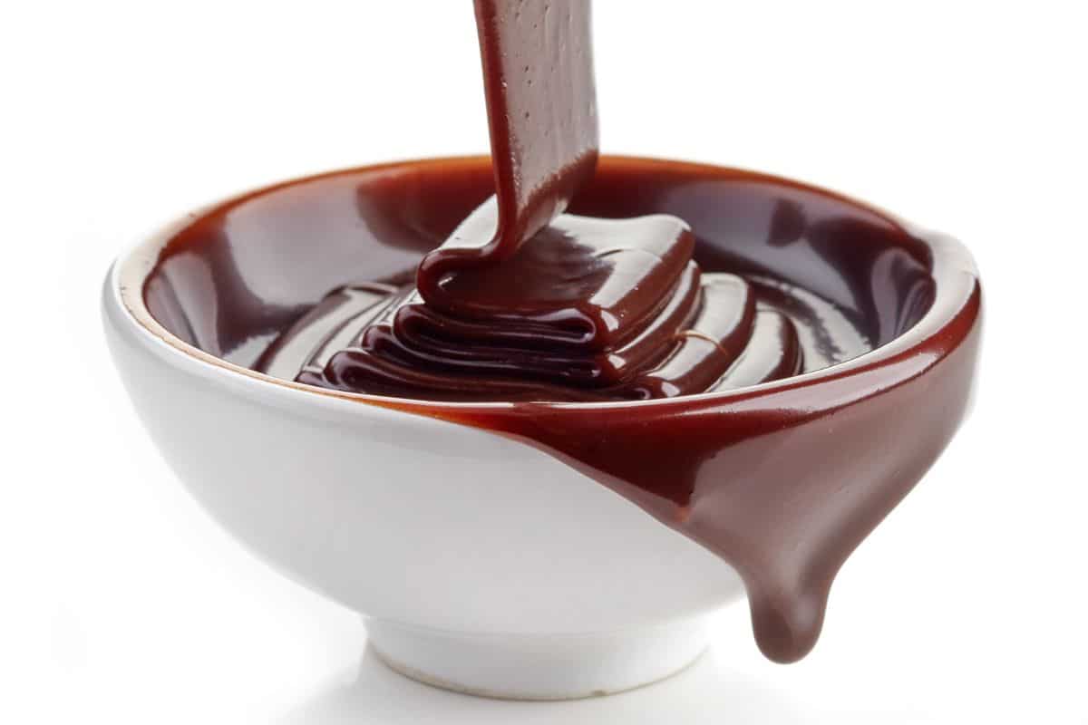 Chocolate syrup being poured into a bowl on a white background.