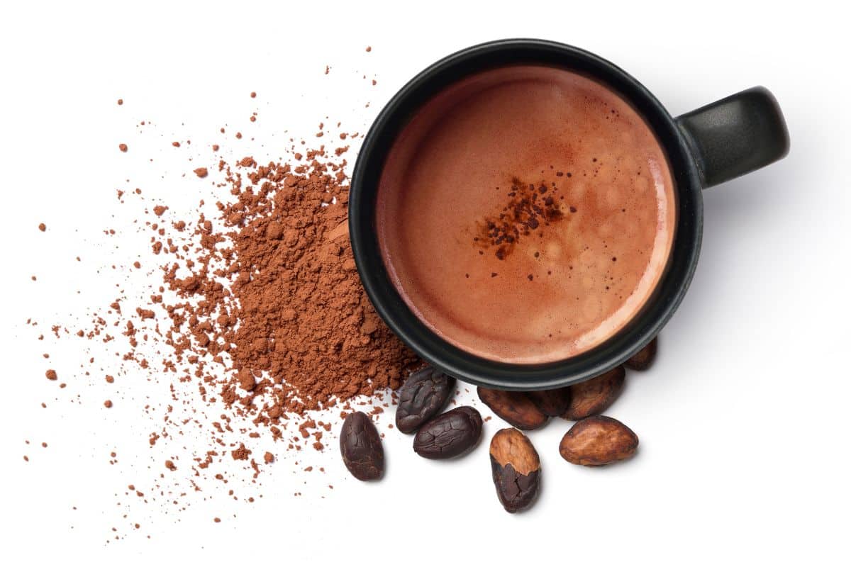 Hot chocolate in a cup next to the mix and cocoa beans on a white background.