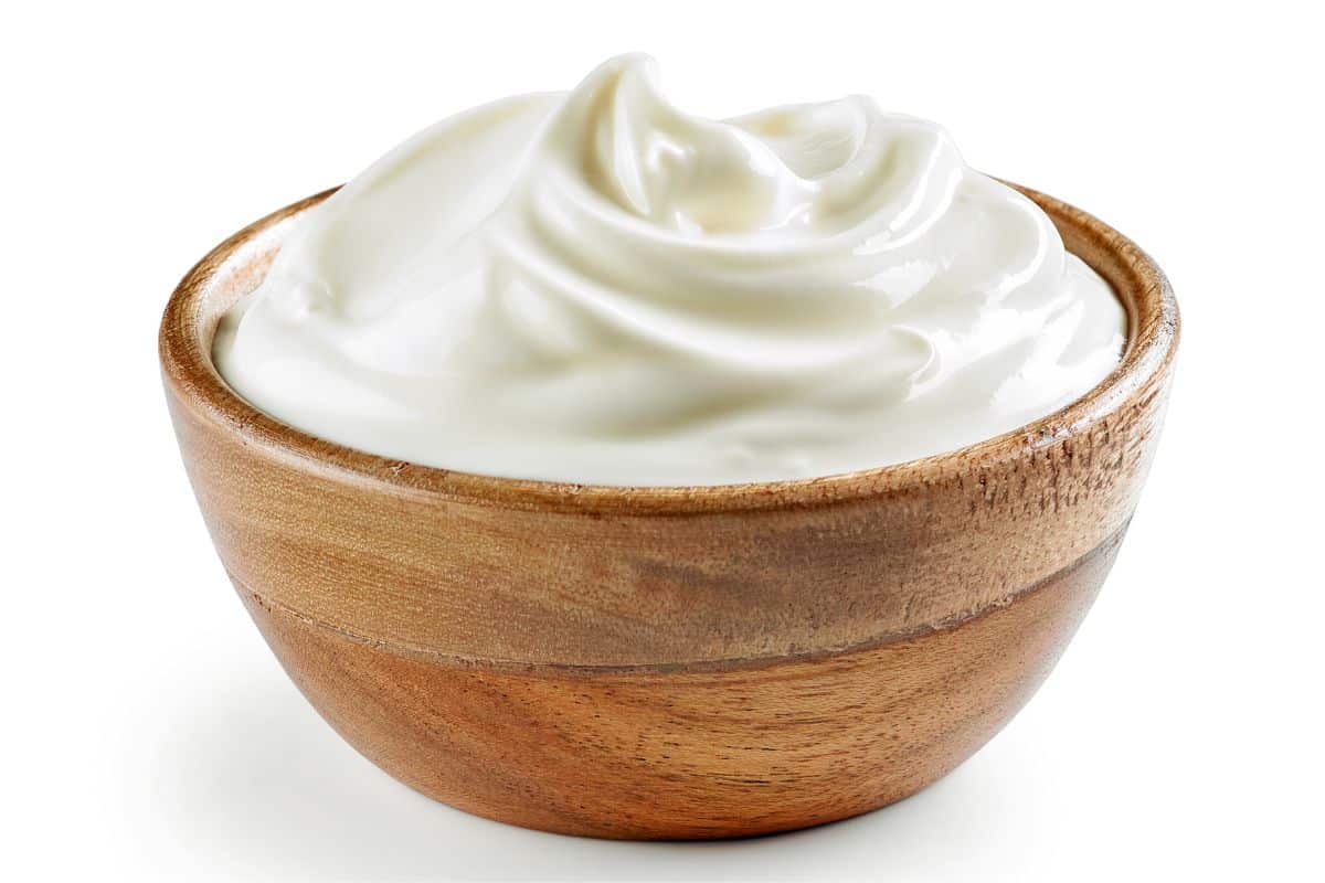 Plain yogurt in a wood bowl on a white background.