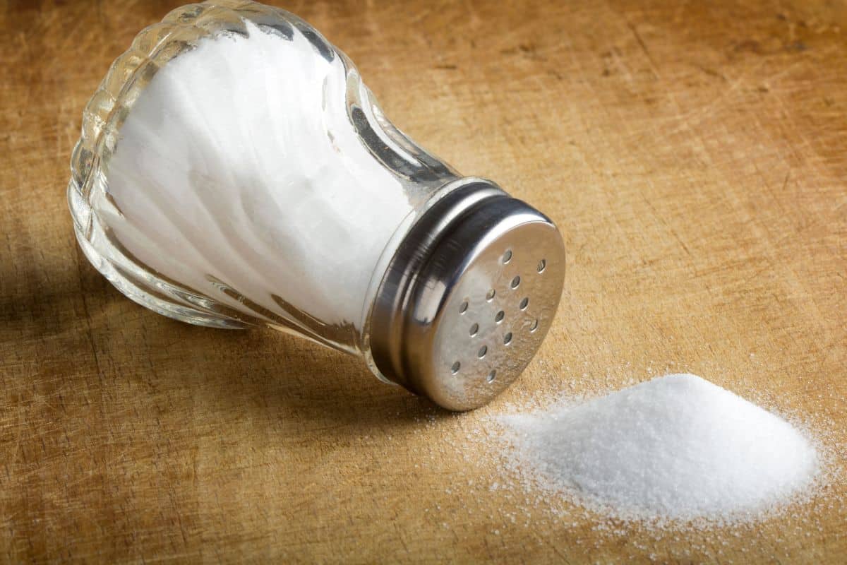 Table salt being poured out of a salt shaker onto a table.