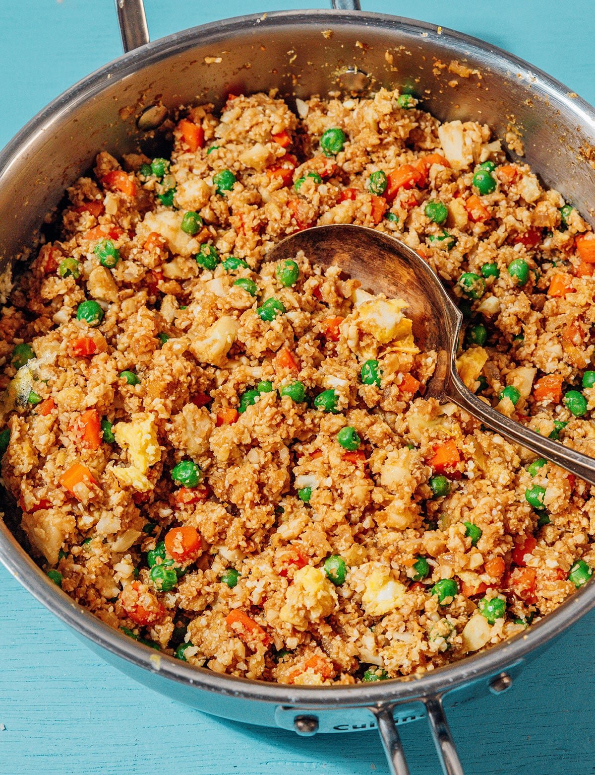 Closeup of cauliflower fried rice in a pan with a serving spoon.