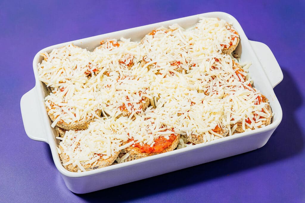 Uncooked eggplant parmesan in a baking dish.