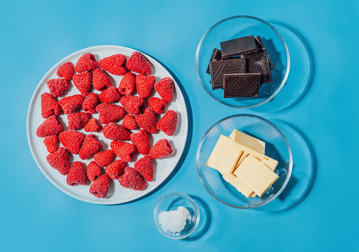 Ingredients for chocolate covered raspberries on a blue background.