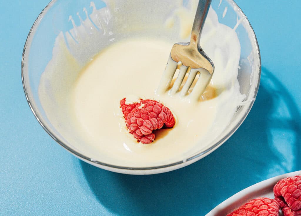 Dipping a raspberry in white chocolate.
