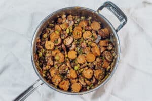 Vegan sausage and mushrooms with holy trinity in a pan.