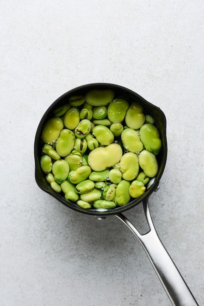 Fava beans blanching in a pot.