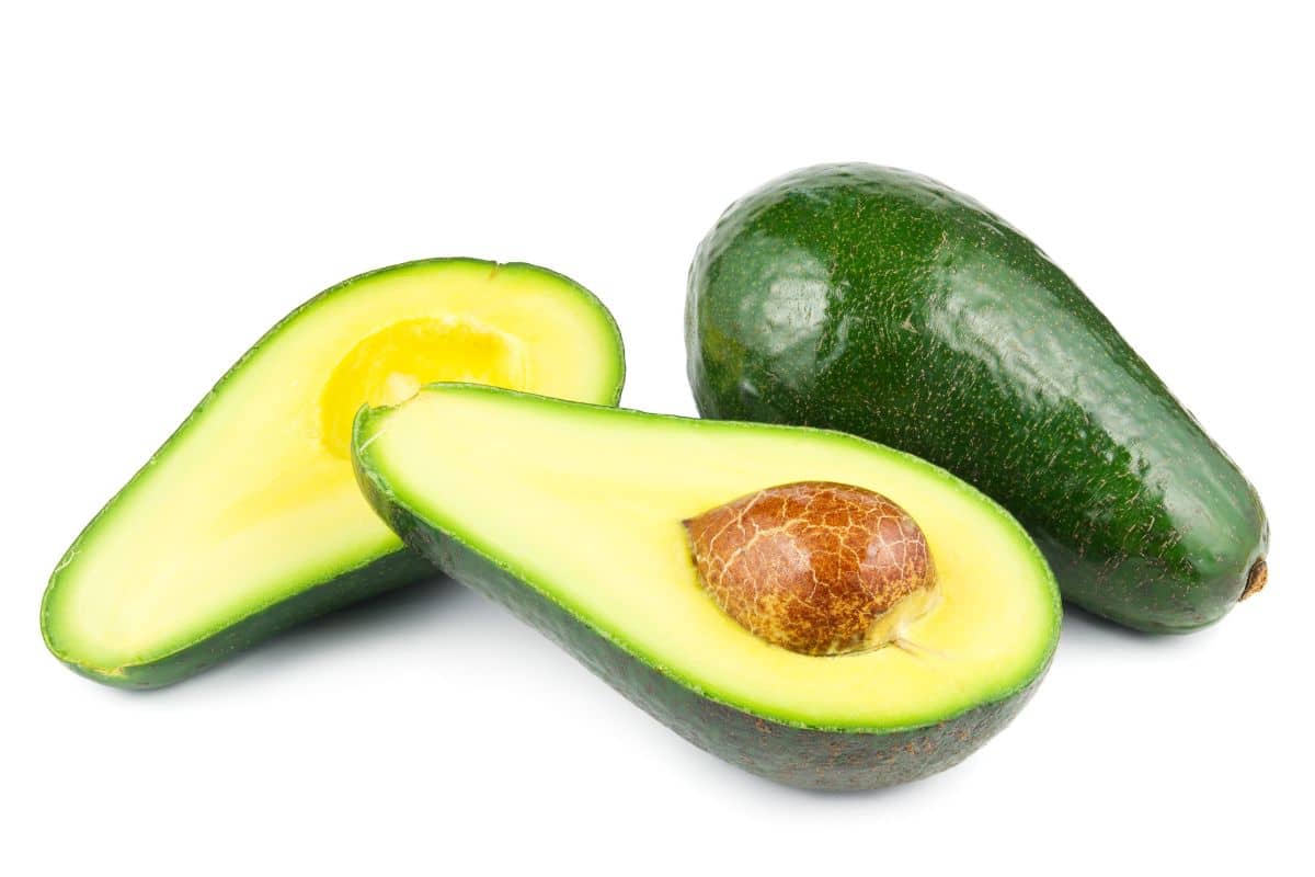 Two fuerte avocados with one cut in half on a white background.