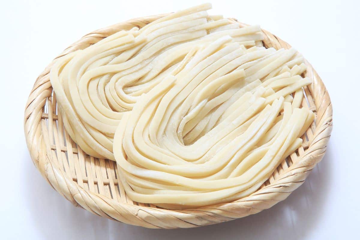 Udon noodles on a wicker plate on a white table.