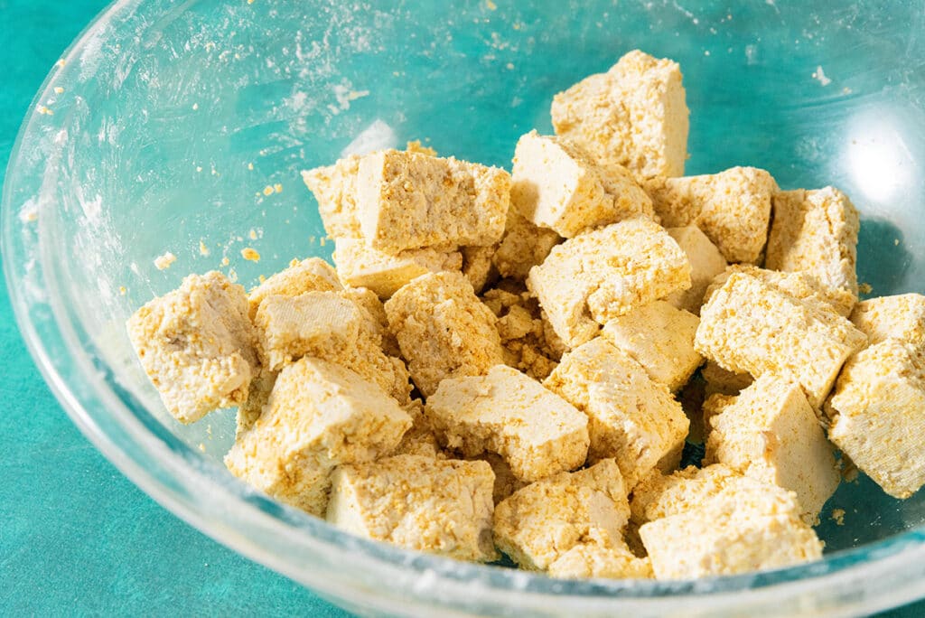 Stirring tofu with seasonings and cornstarch in a bowl.