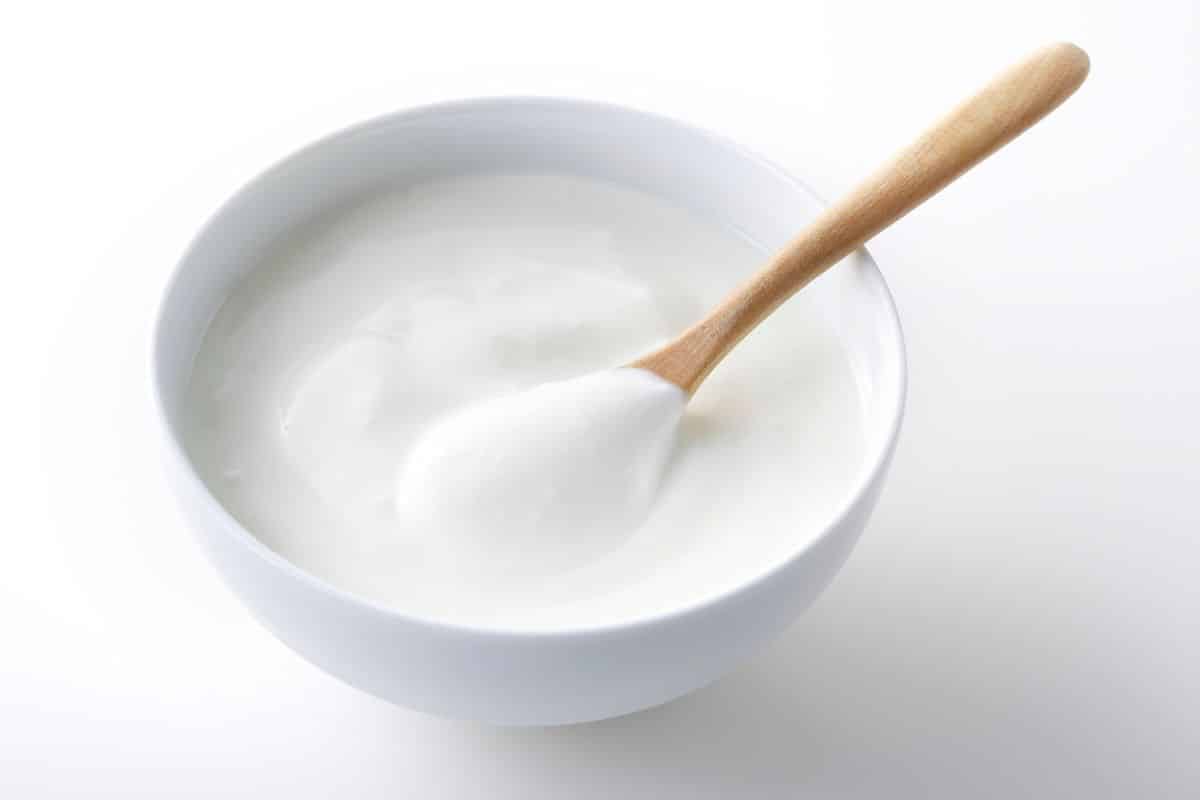 A bowl of almond yogurt with a spoon on a white background.