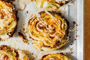 Drizzling tahini dressing on cabbage steaks.