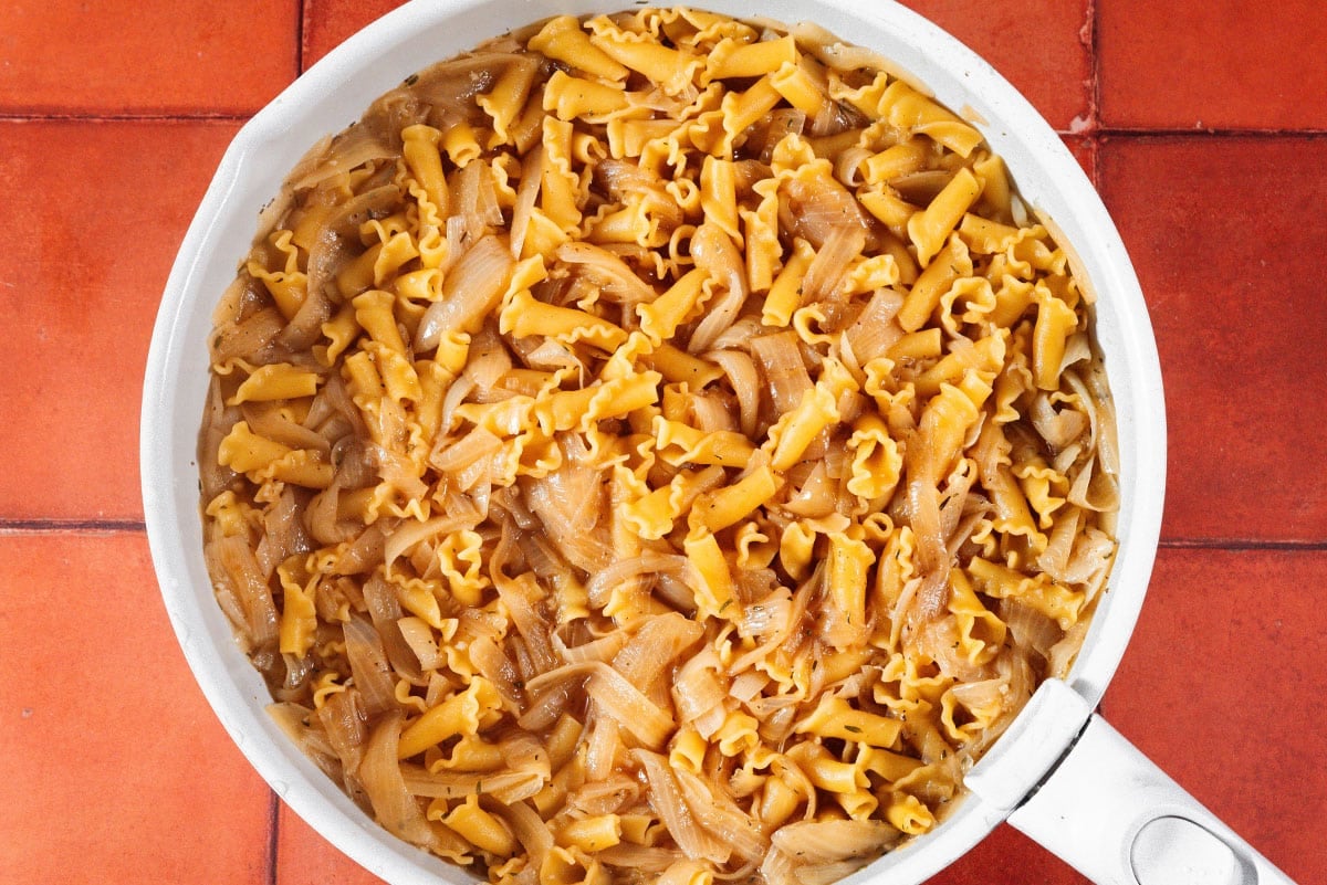 Pasta and broth in a pan with onions.