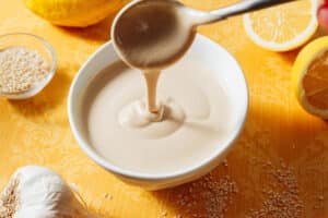 Lemon tahini dressing being stirred with a spoon in a bowl.