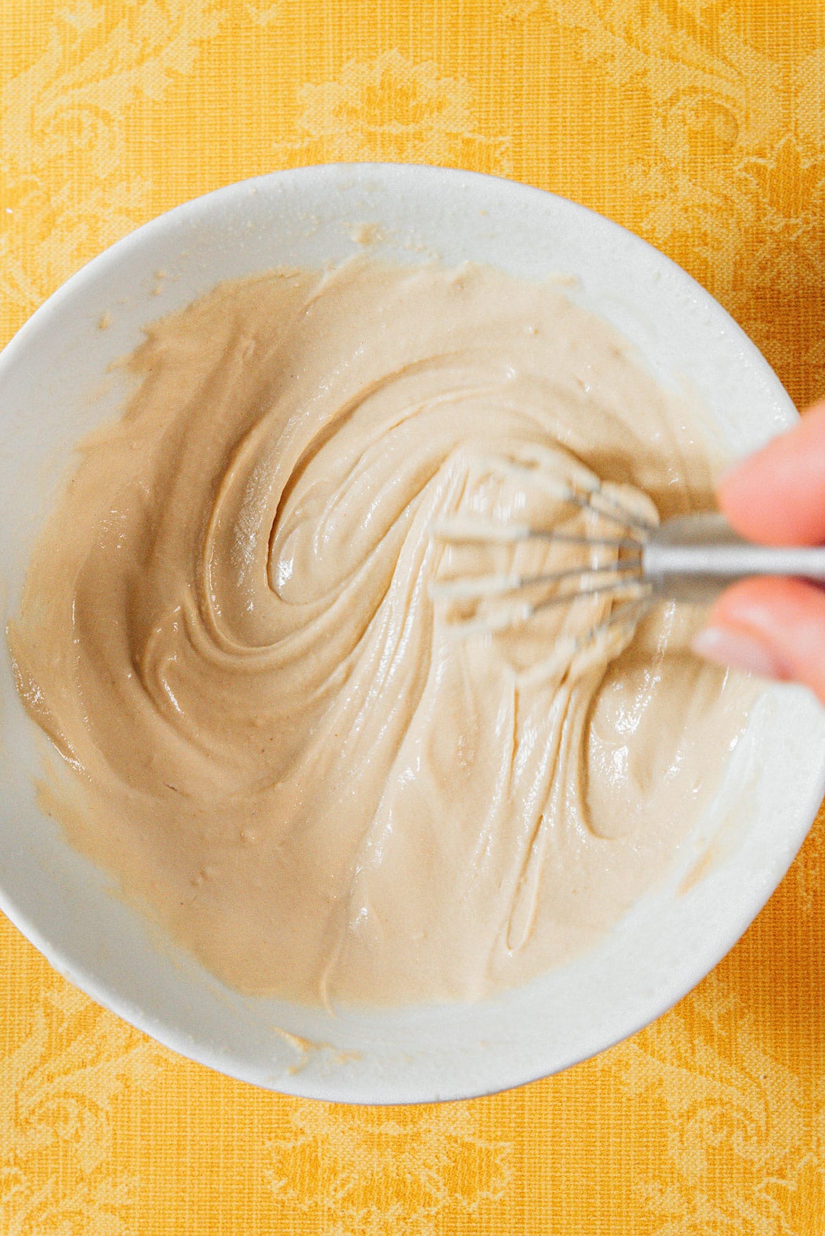 Lemon tahini dressing being stirred with a whisk in a bowl.
