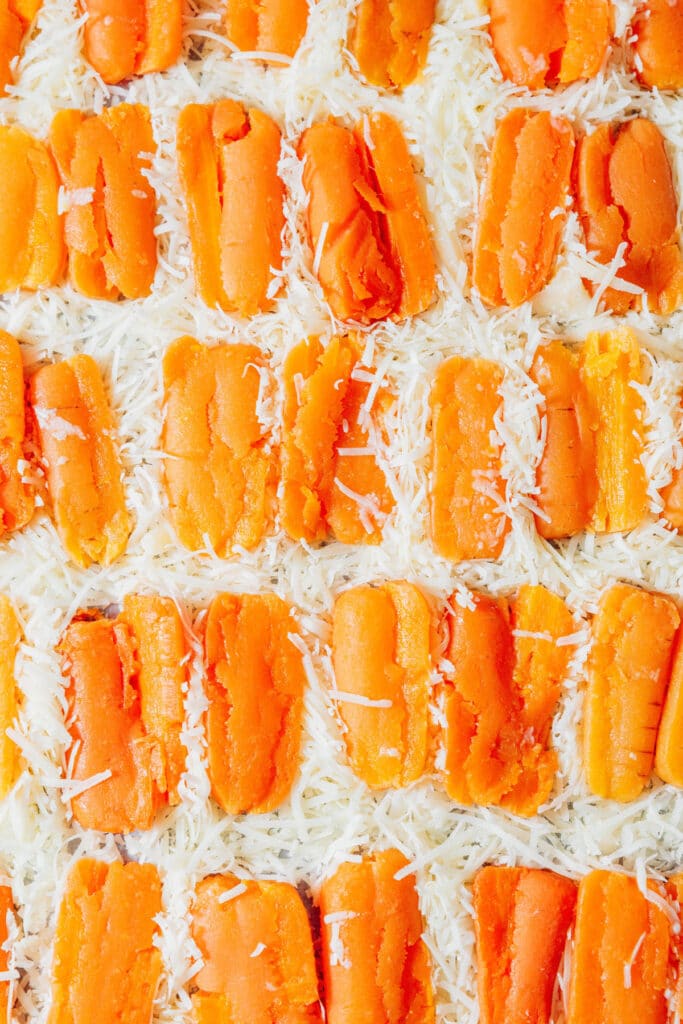 Smashing baby carrots on top of cheese on a baking sheet.