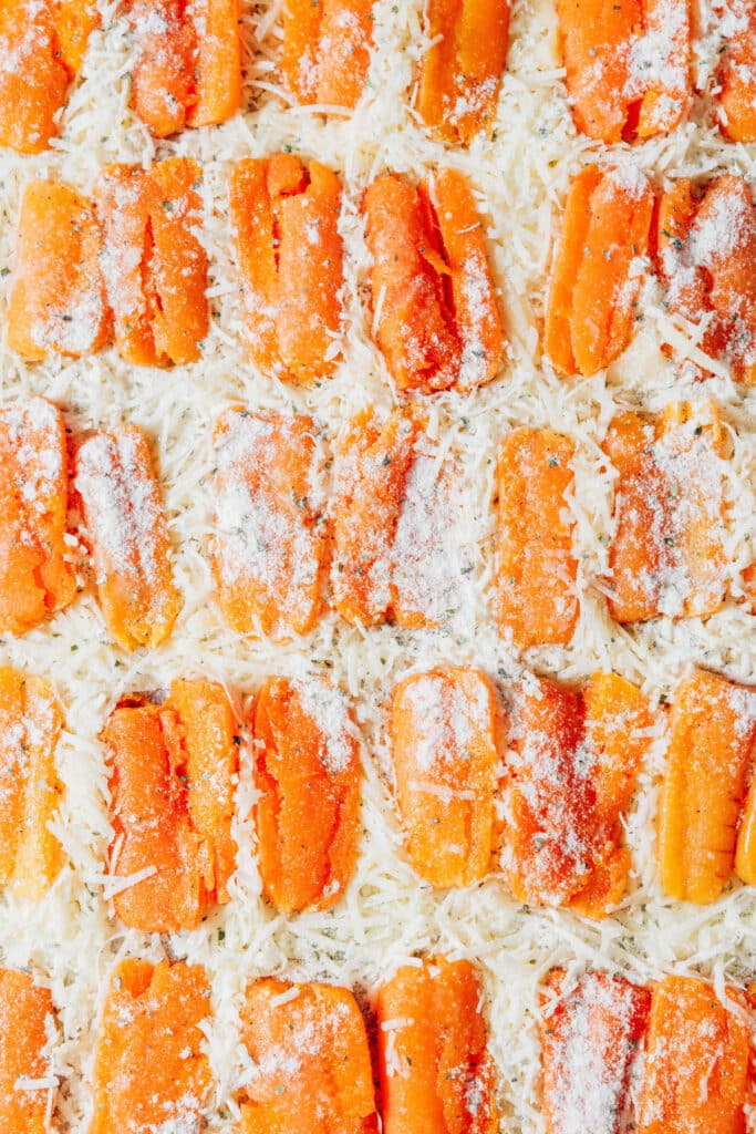 Smashing baby carrots on top of cheese on a baking sheet.