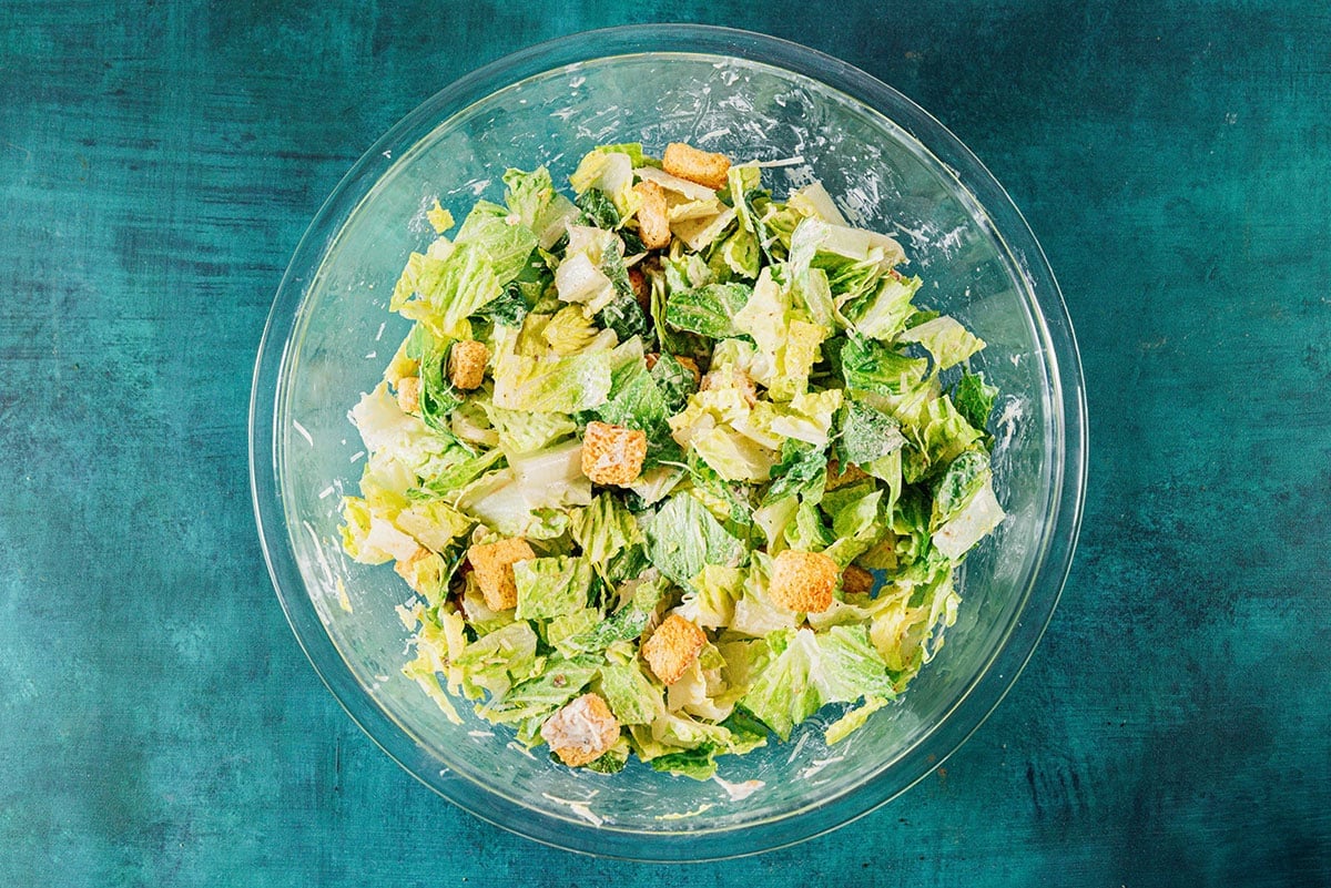 Mixing caesar salad in a glass bowl.