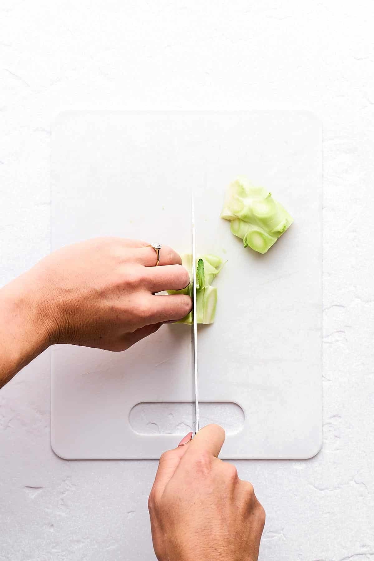 Cutting up a broccoli stem on a cutting board.
