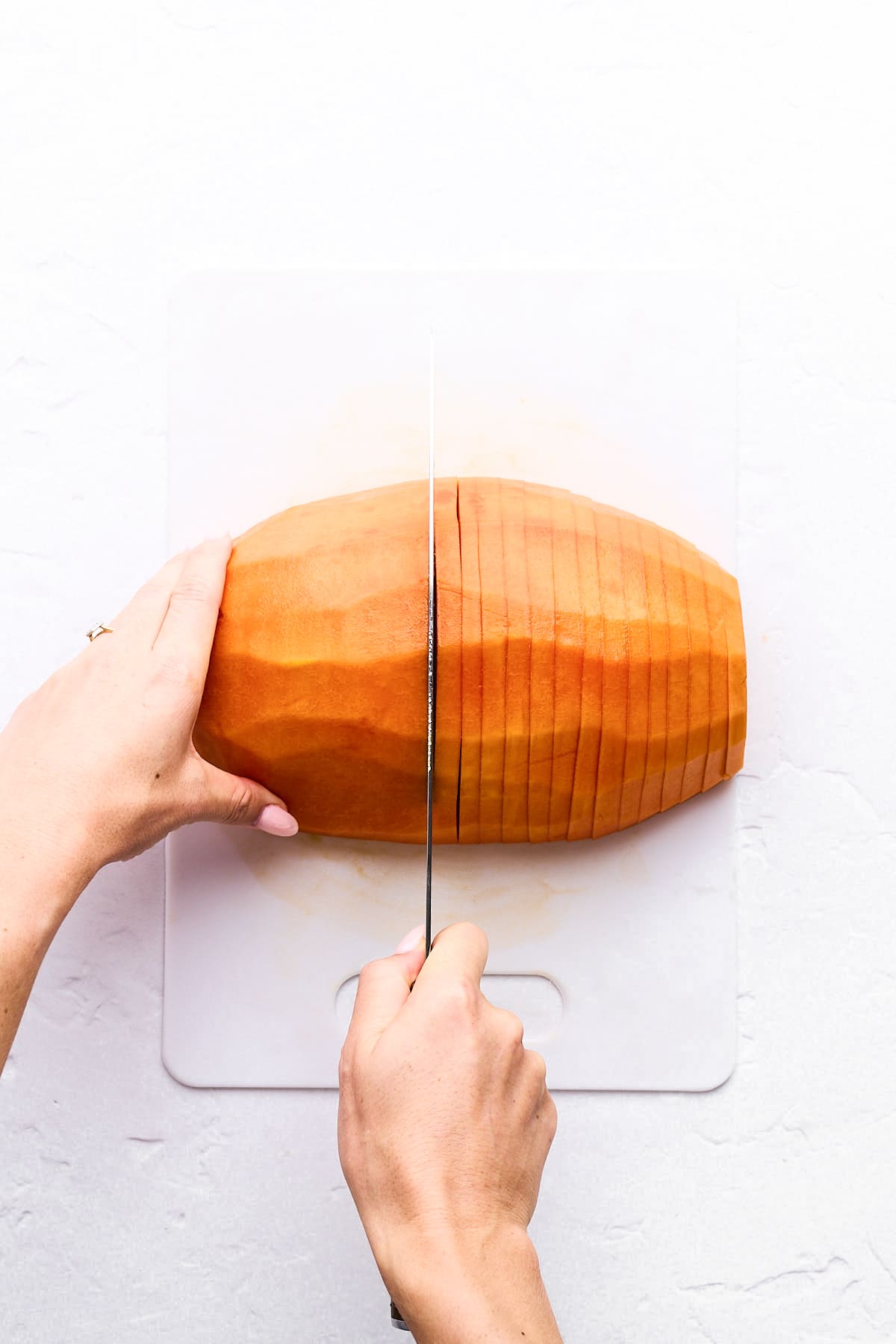 A person slices a peeled sweet potato into even pieces on a white cutting board using a knife, demonstrating knife skills similar to how to cut papaya evenly.