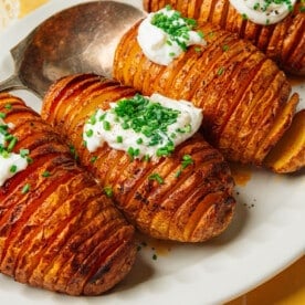 Hasselback potatoes with sour cream and chives on a platter.