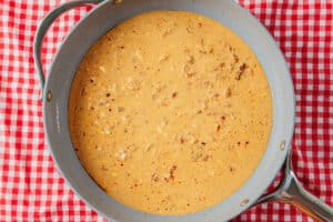 A pan filled with creamy, orange-colored sauce with visible bits of meat, placed on a red and white checkered tablecloth.