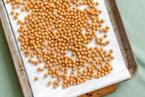 A baking sheet lined with paper towels holds an even layer of chickpeas drying on top of it.