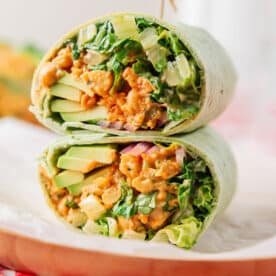 A close-up of a halved wrap filled with leafy greens, sliced avocado, and a creamy, textured filling, placed on parchment paper.