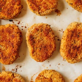 Nine breaded, baked chickpea nuggets are arranged on a sheet of parchment paper, spaced evenly in rows. The patties have a golden-brown, crispy coating.