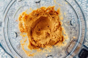 Thick, blended mixture with a light brown color inside a clear food processor bowl, seen from above.
