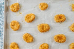 Baked breaded nuggets arranged on a parchment-lined baking sheet.