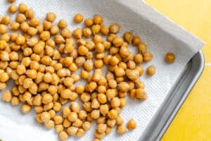 Cooked chickpeas spread out on a paper towel-lined baking sheet, drying.