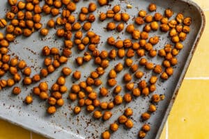 Roasted chickpeas coated with spices are spread out on a gray baking sheet.