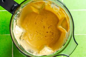 Top view of a blender containing a creamy, light brown mixture on a green tiled surface.