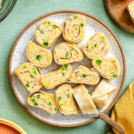 A plate of sliced chickpea roll-ups filled with cheese and chopped green peppers, arranged neatly on a speckled plate with a serving spatula on the side.