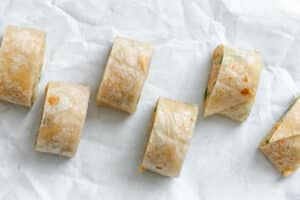 Six pieces of rolled flatbread with a visible filling are arranged in a diagonal pattern on a crumpled white surface.