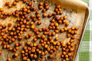 Roasted chickpeas scattered on a parchment-lined baking sheet, showing a golden brown and slightly crispy texture.