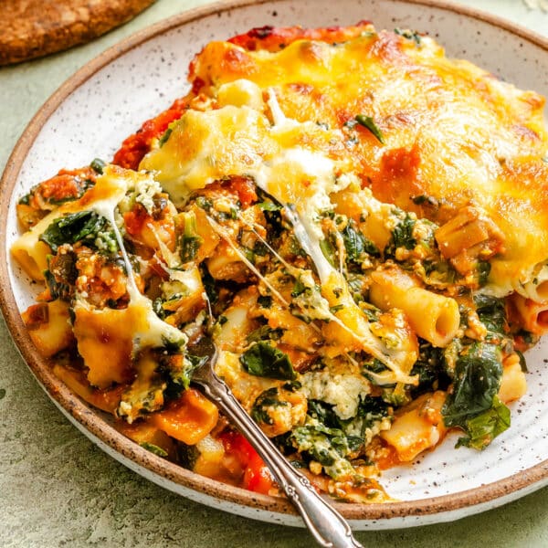 A plate of baked ziti with spinach, ricotta, tomato sauce, and melted cheese, with a fork resting on the side.