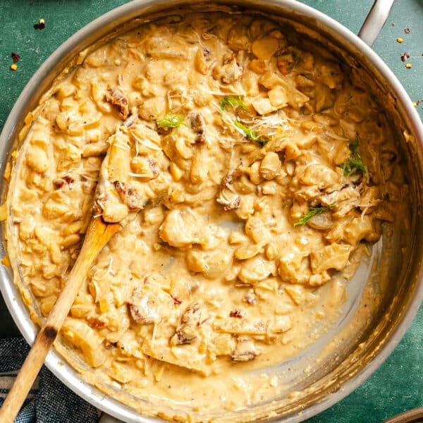 A skillet filled with braised butter beans mixed with pieces of meat, vegetables, and braised beans, with a wooden spoon resting inside.