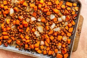 A baking sheet with roasted chickpeas, diced sweet potatoes, and chopped onions on a light-colored surface.
