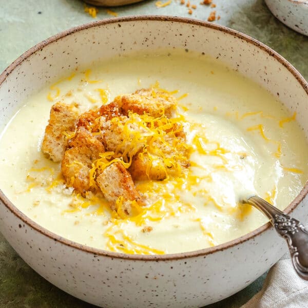 A bowl of creamy cauliflower soup topped with croutons and shredded cheese, with a spoon resting inside the bowl.