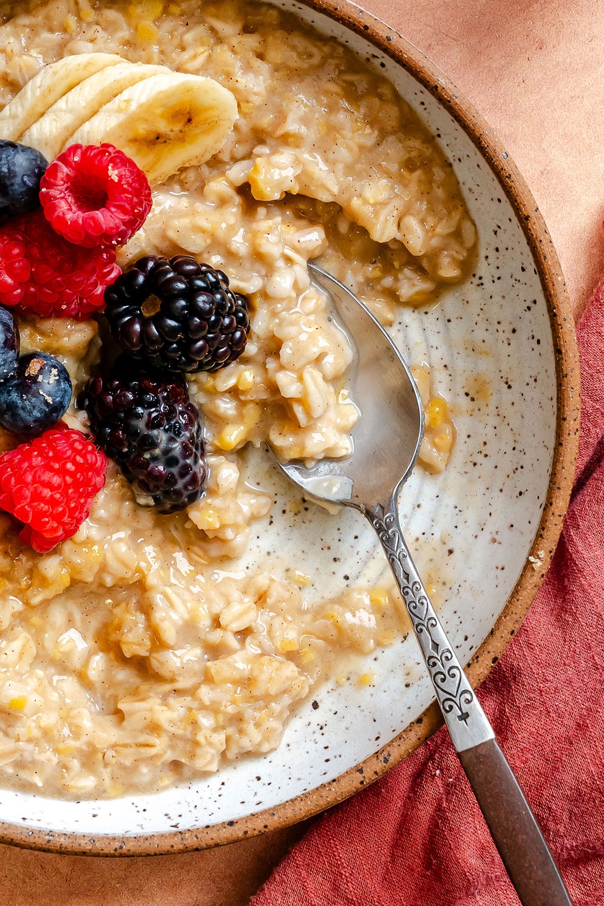 Bowl of chickpea oatmeal topped with banana slices, raspberries, blueberries, and a blackberry, with a spoon resting in the bowl on a brown napkin.