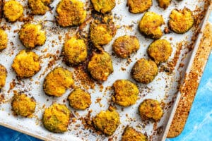 Baked, seasoned smashed potatoes spread on a parchment-lined baking sheet, with crispy edges and a golden-brown coating.