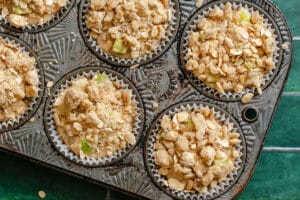A close-up of a muffin tin filled with unbaked muffins topped with crumbly oat and nut streusel, ready to be baked.