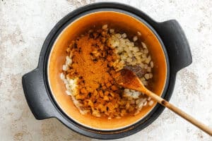 Overhead view of chopped onions and spices in a large pot with a wooden spoon, ready for cooking.