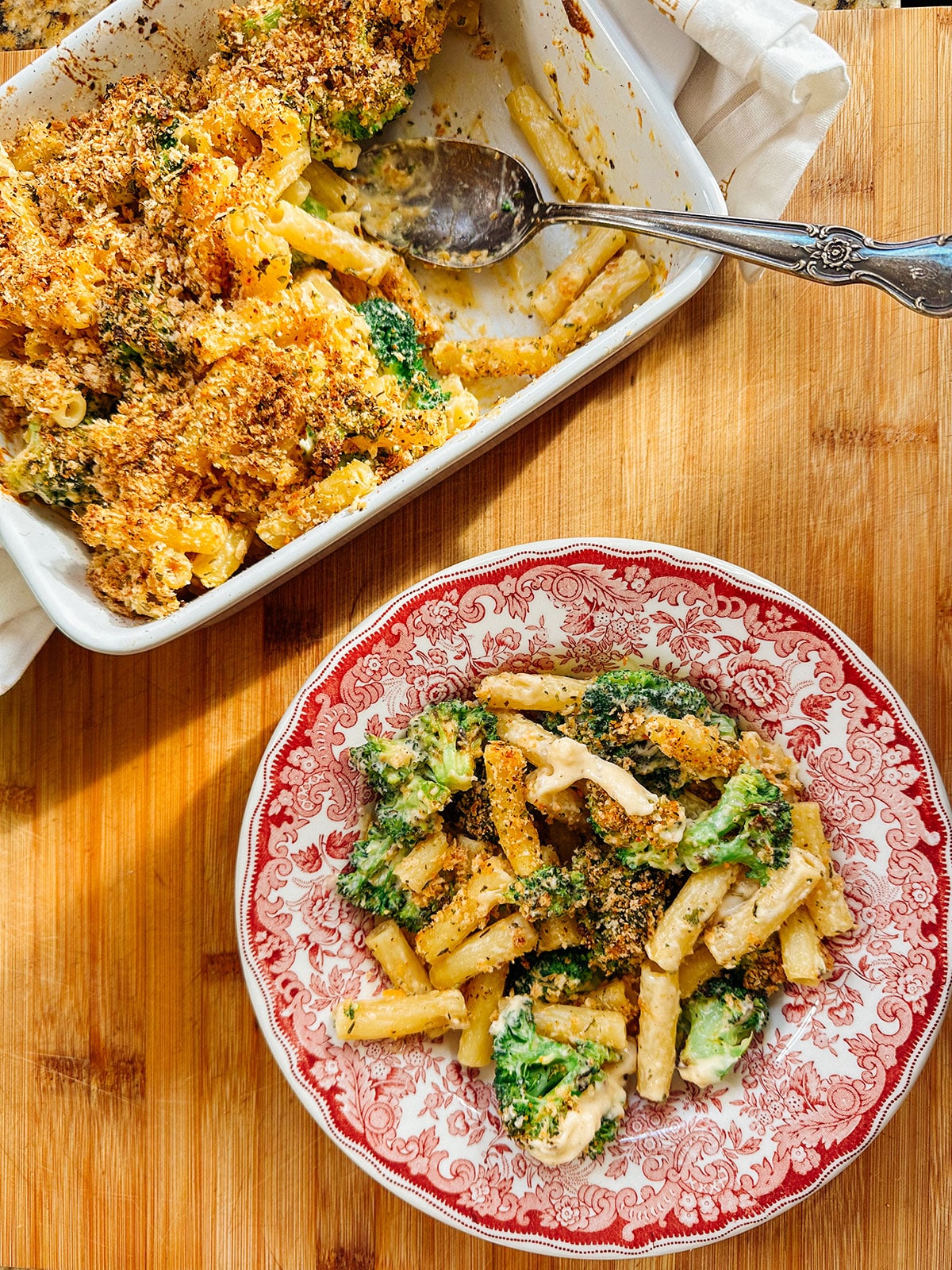 A serving of baked pasta with broccoli and breadcrumbs on a decorative plate, with the baking dish and serving spoon nearby on a wooden surface—just the kind of comforting meal you’d find in a Hungryroot selection according to a recent nutritionist review.