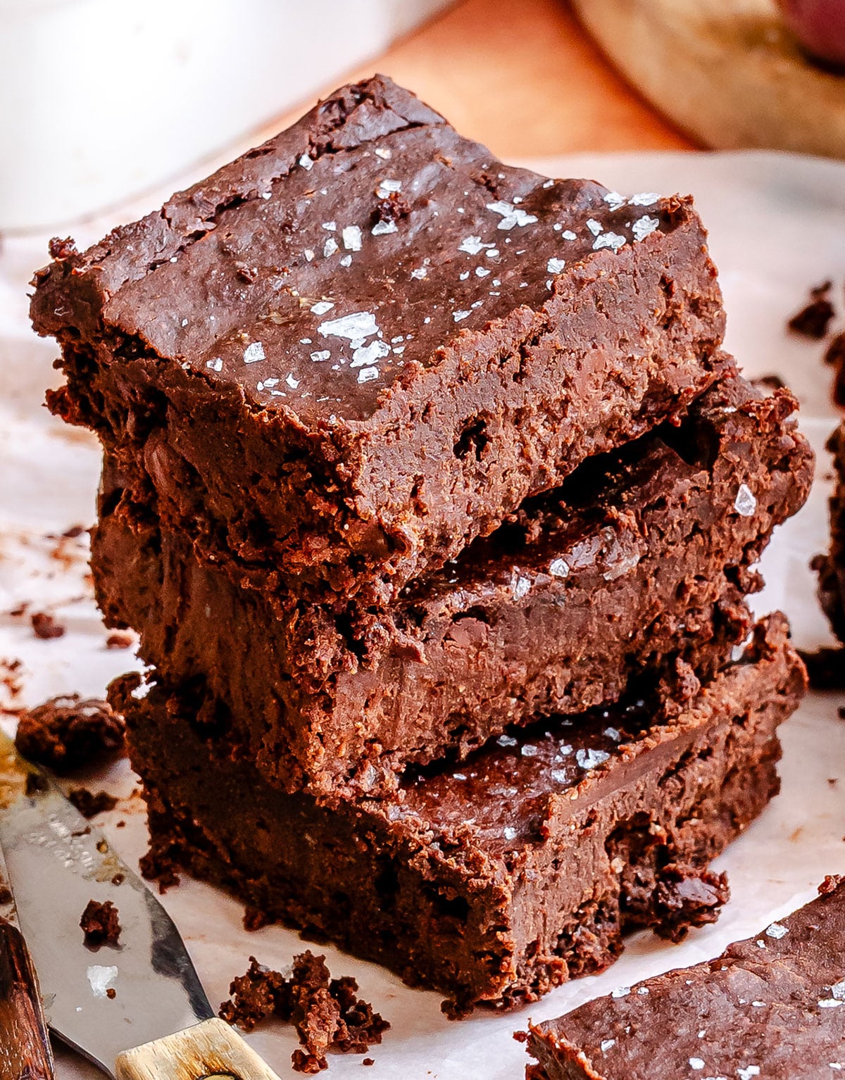 A stack of three thick, fudgy chocolate brownies topped with sea salt flakes, resting on parchment paper.