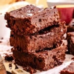 A stack of three thick, fudgy Sweet Potato Brownies with a slightly crumbly texture, placed on parchment paper.