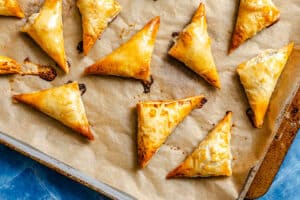 Triangular pastries with golden, flaky crusts are arranged on a parchment-lined baking sheet.
