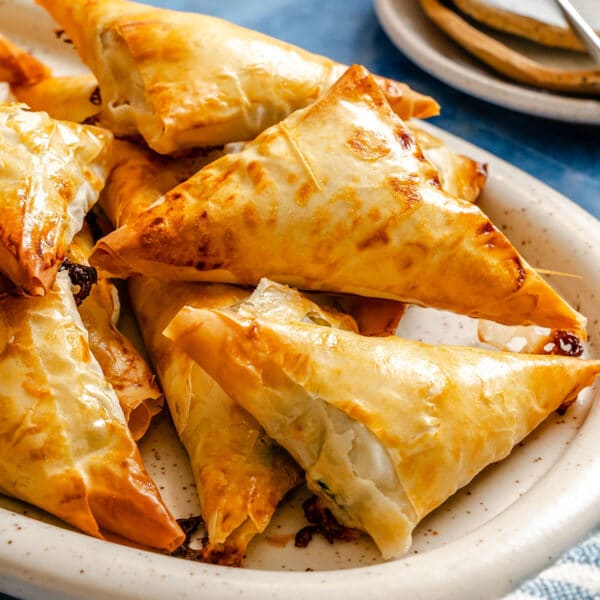 A plate of golden-brown, triangular pastry turnovers, arranged in a pile on a white oval dish.